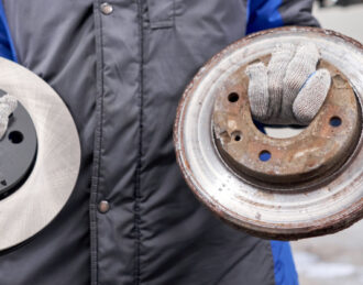 Mechanic holds old rusty brake disc and new disc at a brake shop near me
