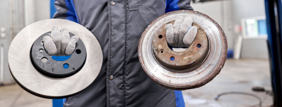 Mechanic holds old rusty brake disc and new disc at a brake shop near me
